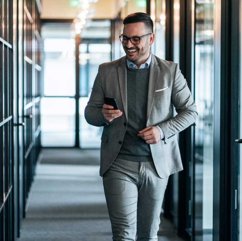 man walking through the office on his phone with a smile